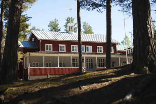 Pörkenäs lägergård, röd byggnad omgiven av höga tallar, en solig sommardag.