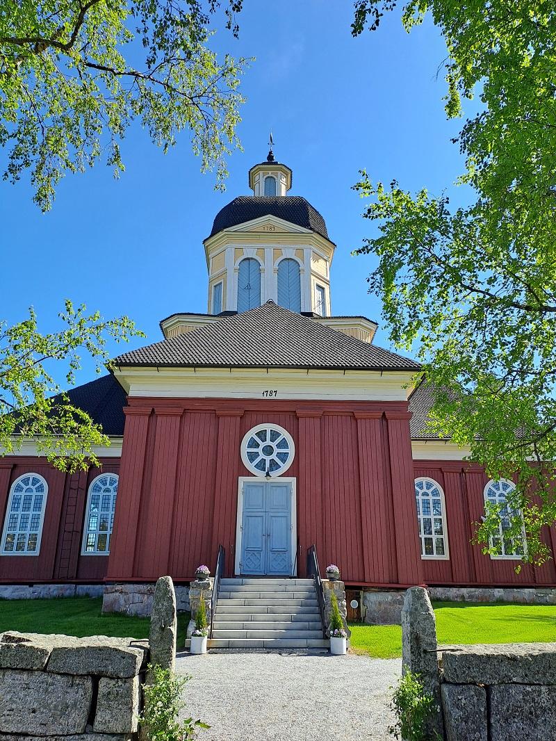 Larsmo kyrka en solig sommardag. Björkgrenar syns i förgrunden.